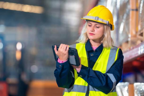 an woman wearing a hard hat and safety vest while looking at her tablet